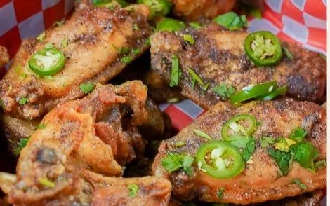 Crispy chicken wings with sliced jalapeño and herbs on red-checkered paper
